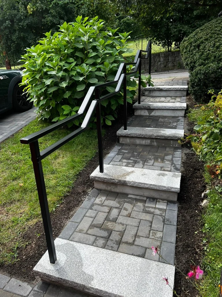 Black front step railing installed beside landscaping