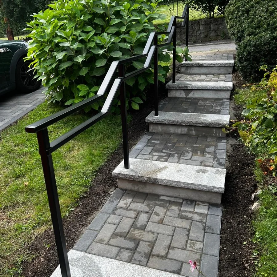 Black front step railing installed beside landscaping
